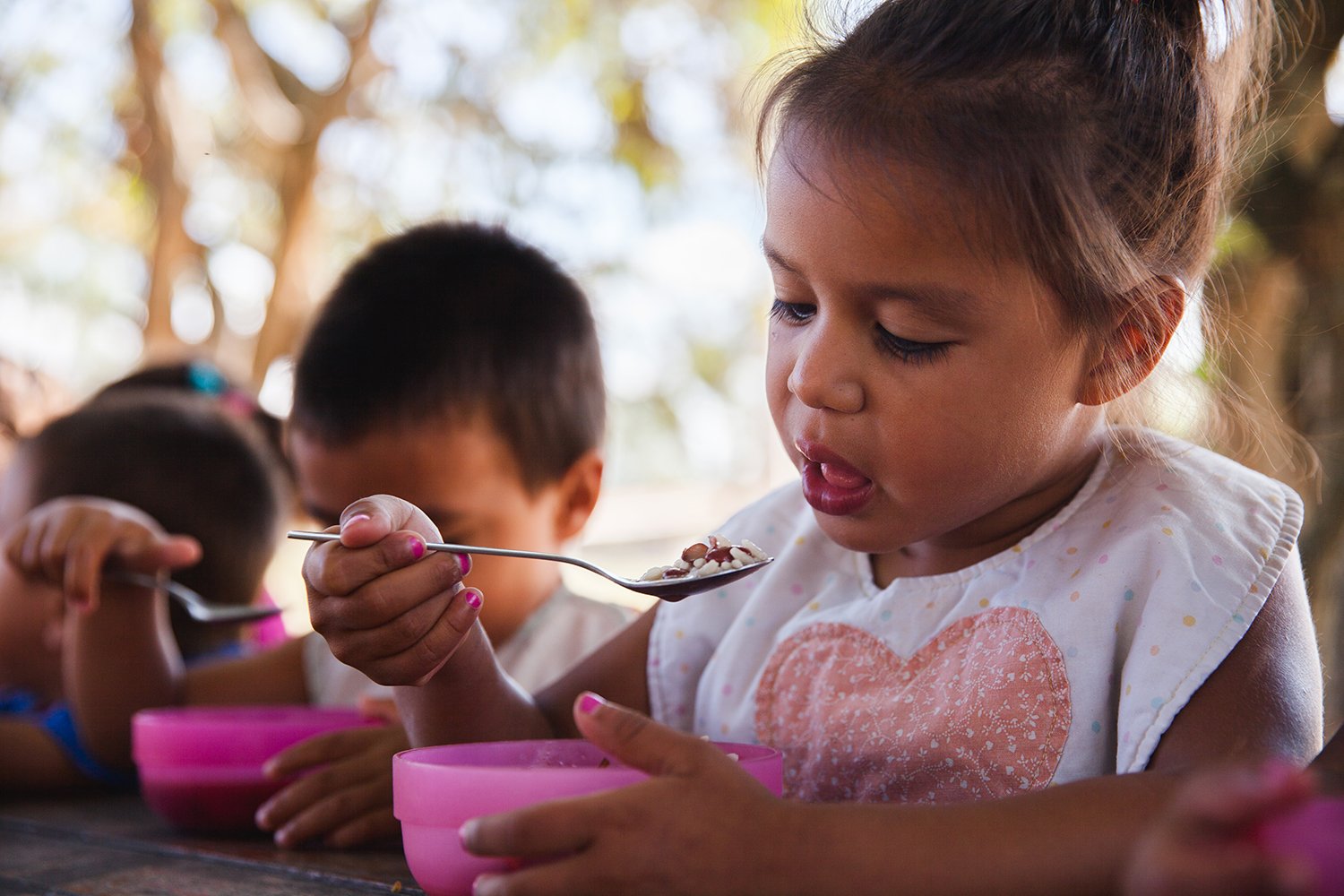 Niña levantando una cuchara de comida a la boca.