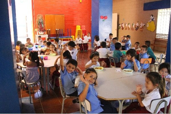 Kids sitting at a table waving, El Salvador